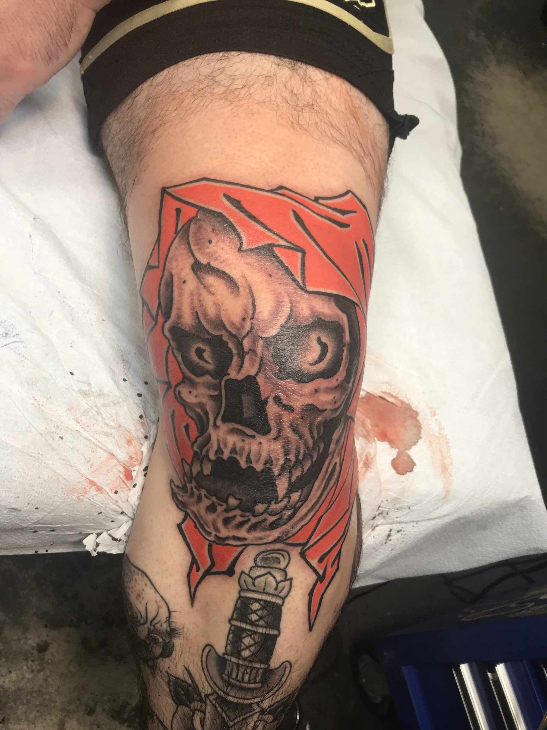 Wider front view of the fresh knee reaper with the surrounding leg tattoos.